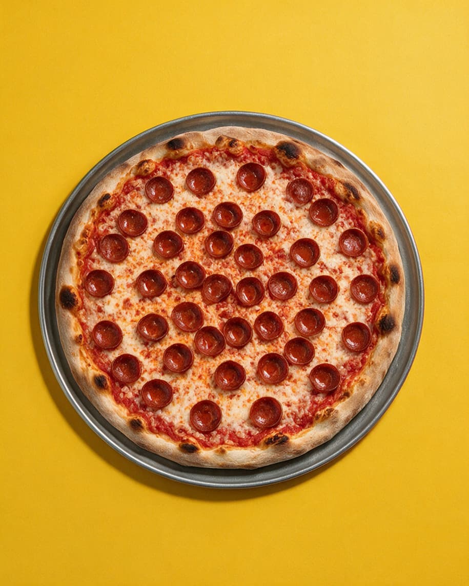 Whole pepperoni pizza and metal tray seen from above on a yellow background