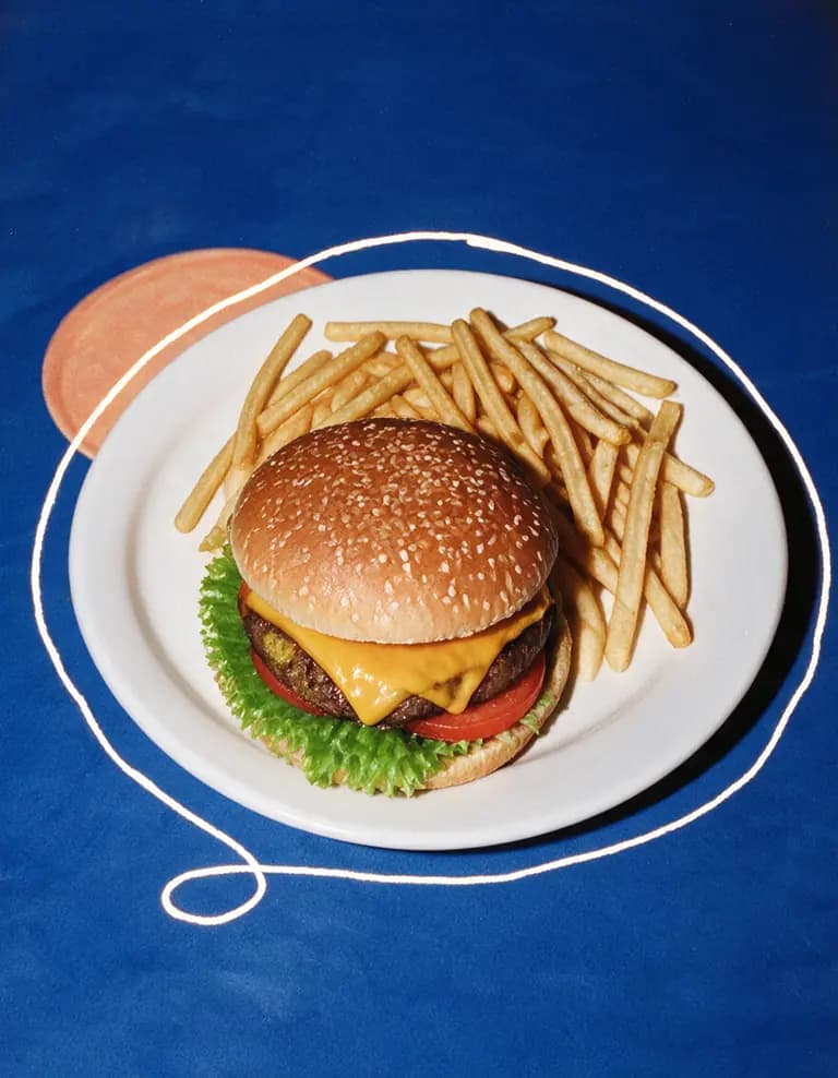 Cheeseburger and fries on a white plate against a deep blue background