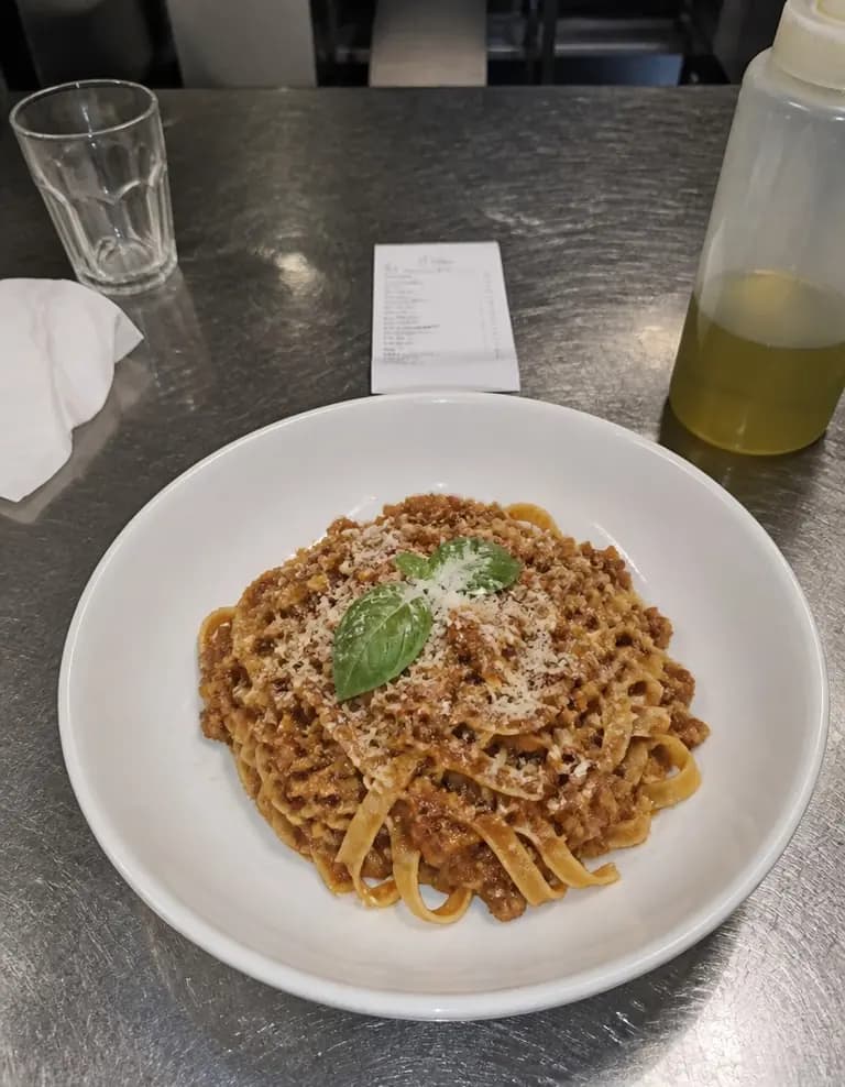 Tagliatelle with ragù in a white bowl on a stainless steel counter